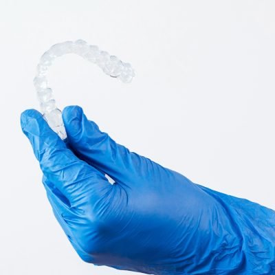 Adult man with gloves holds invisalign transparent braces for dental correction. Caucasian person holding invisible orthodontic retainer and aligner with white copy space.